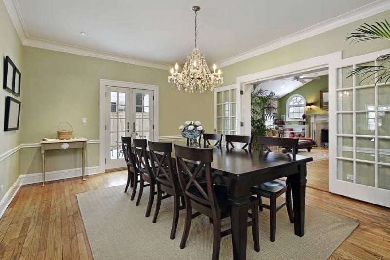 Chic cottage dining room features a farmhouse dining table lined with black  salt Chairs illuminated by a Thomas O'Brien Bryant Chandelier